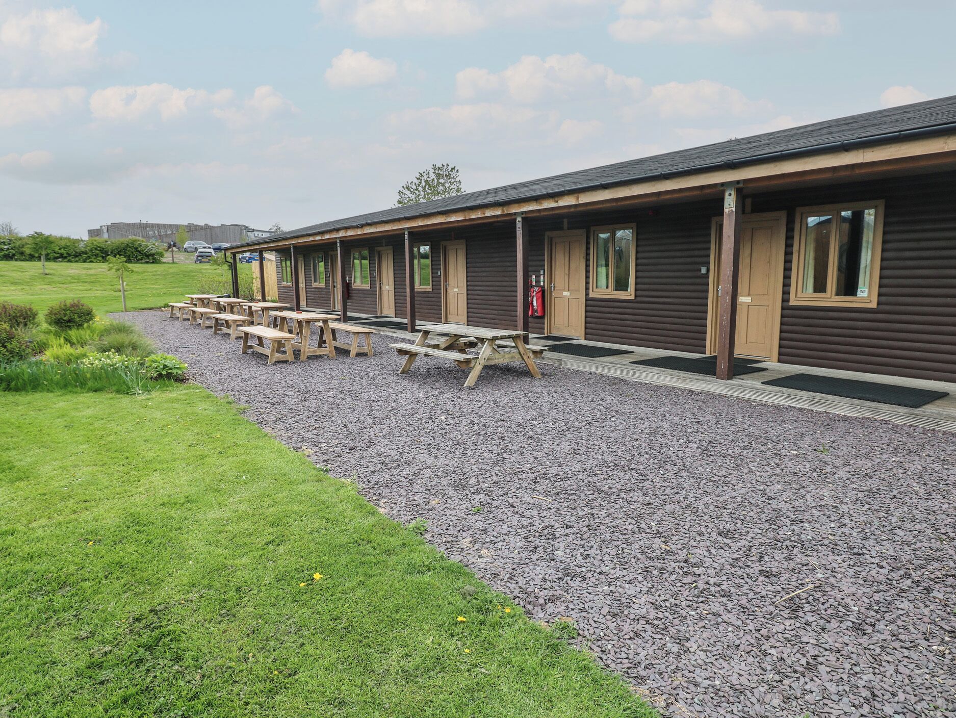 A row of wooden cabins with picnic tables in front, set in a grassy area with gravel paths.