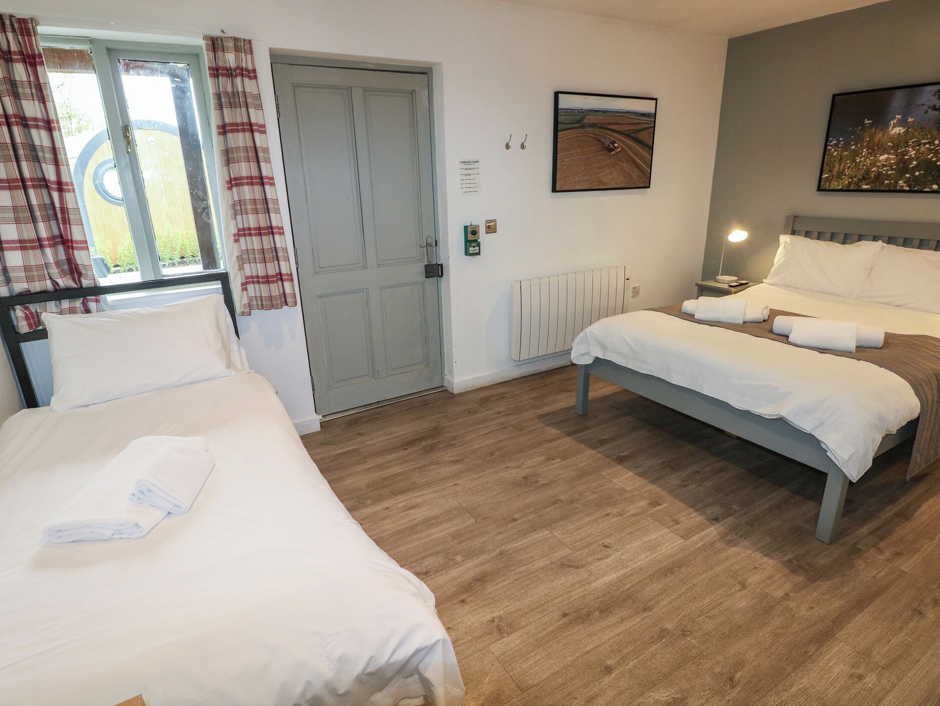 A hotel room with two single beds, a radiator, a framed picture on the wall, and a window with curtains.