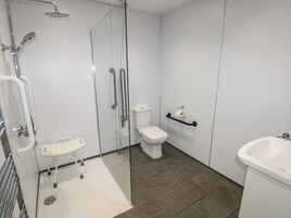 Un baño moderno con ducha de vidrio, inodoro blanco, barra de apoyo y lavamanos.