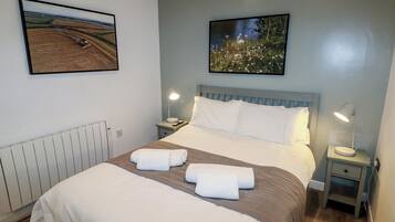 A hotel room with a large bed, two bedside tables, a nightstand, a radiator, and two framed pictures on the walls.