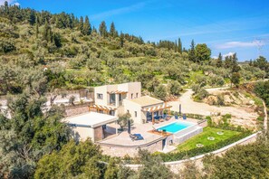 Eine moderne Villa mit Pool, umgeben von üppiger Vegetation und Hügeln.