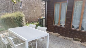 Una mesa blanca con cuatro sillas en una zona de grava, un muro de piedra y un edificio de madera con ventanas.
