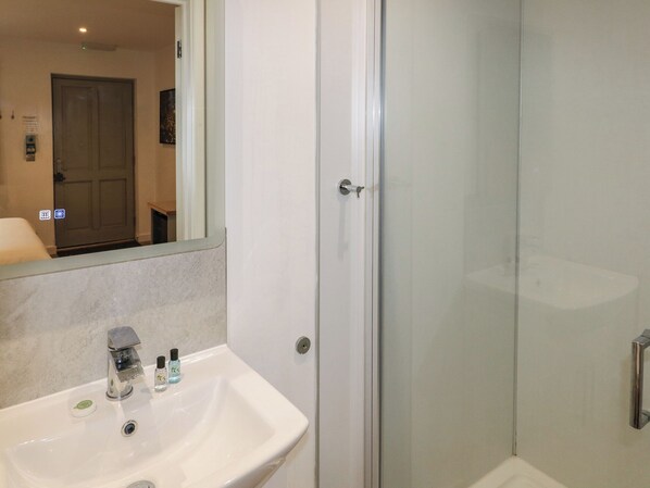 A bathroom with a sink, mirror, and glass shower enclosure. - Alder (Cowbridge)