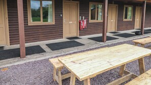 Una hilera de cabañas de madera con un porche cubierto, mobiliario exterior y un pequeño jardín.