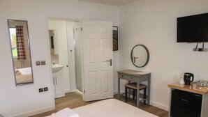 Habitación de hotel con cama, escritorio, espejo, televisión y baño visible a través de una puerta abierta.