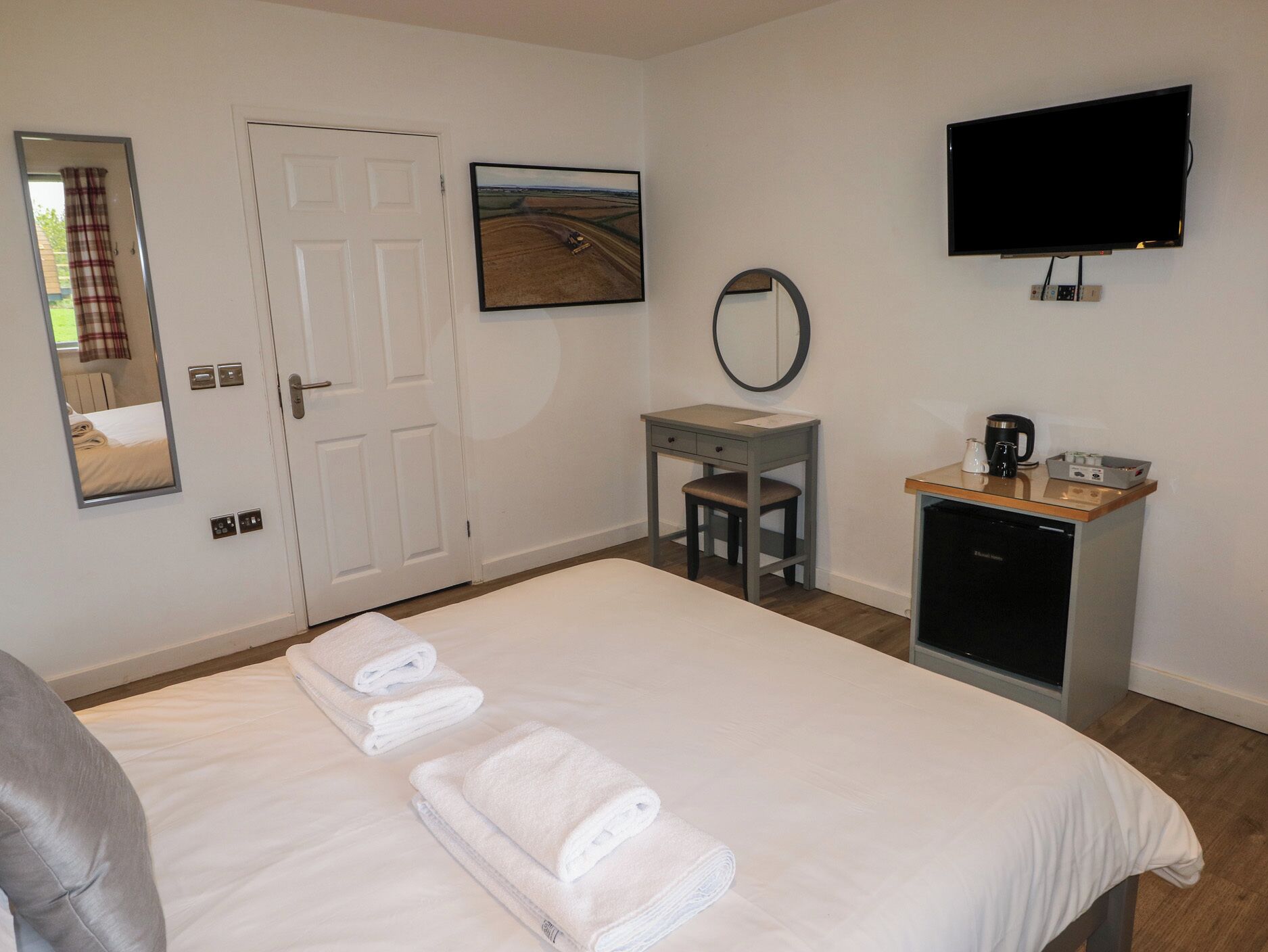 A hotel room with a bed, a desk, a chair, a television, and a mirror.
