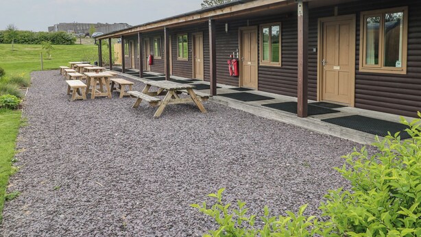 Una hilera de habitaciones de estilo cabaña de troncos con mesas de picnic al frente.