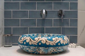 A bathroom with a blue tiled wall, a round sink with floral patterns, and two faucets.