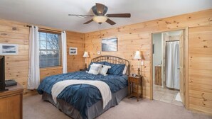 Une chambre à coucher avec un lit, un ventilateur de plafond, une fenêtre avec des rideaux, une porte et un mur en bois.