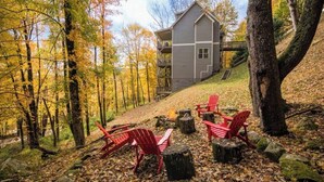 Un chalet doté d’un balcon, entouré d’arbres aux couleurs automnales, et d’un espace extérieur avec un foyer.