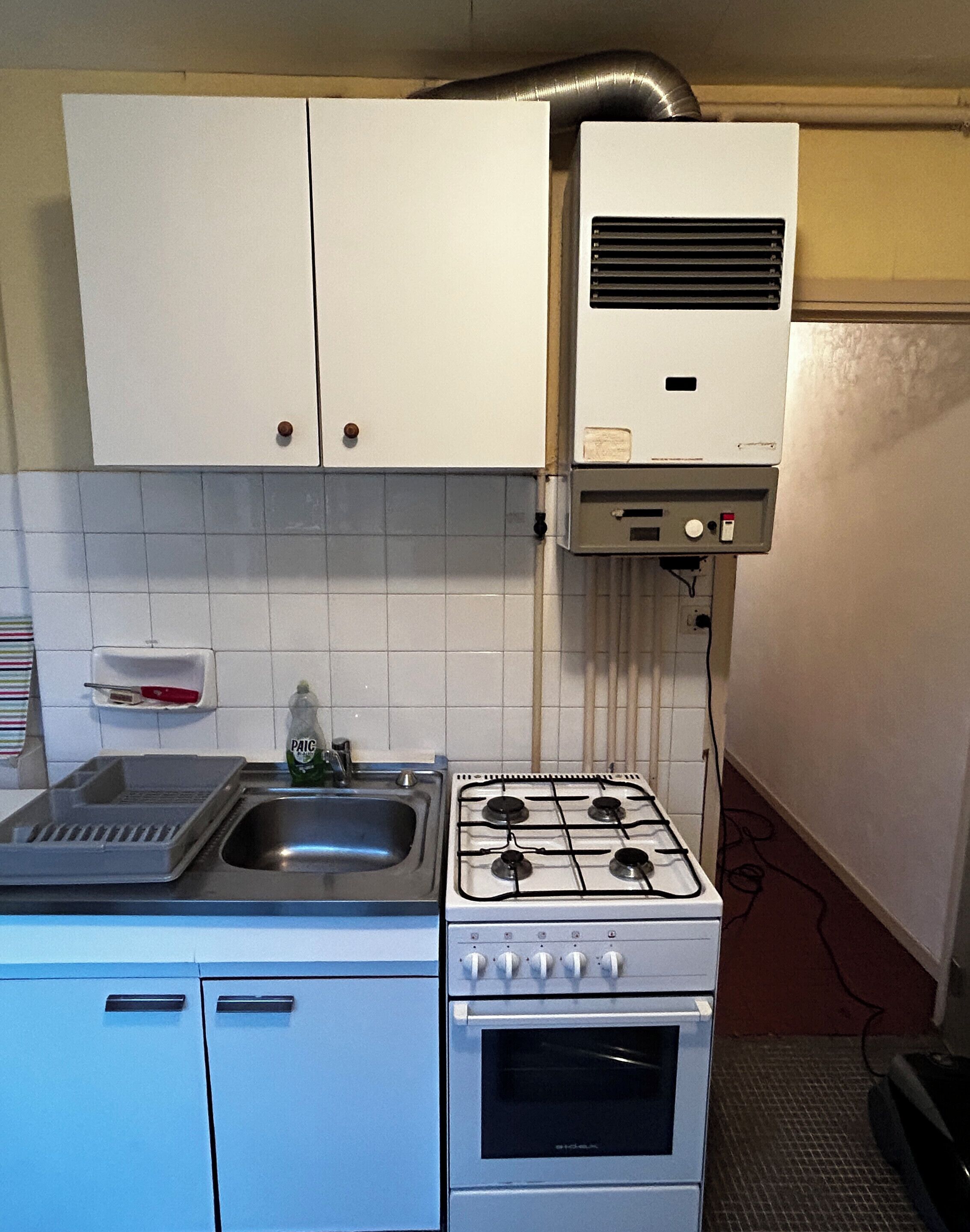 Une cuisine de taille réduite, avec des meubles blancs, une cuisinière à gaz, un évier et un égouttoir à vaisselle.