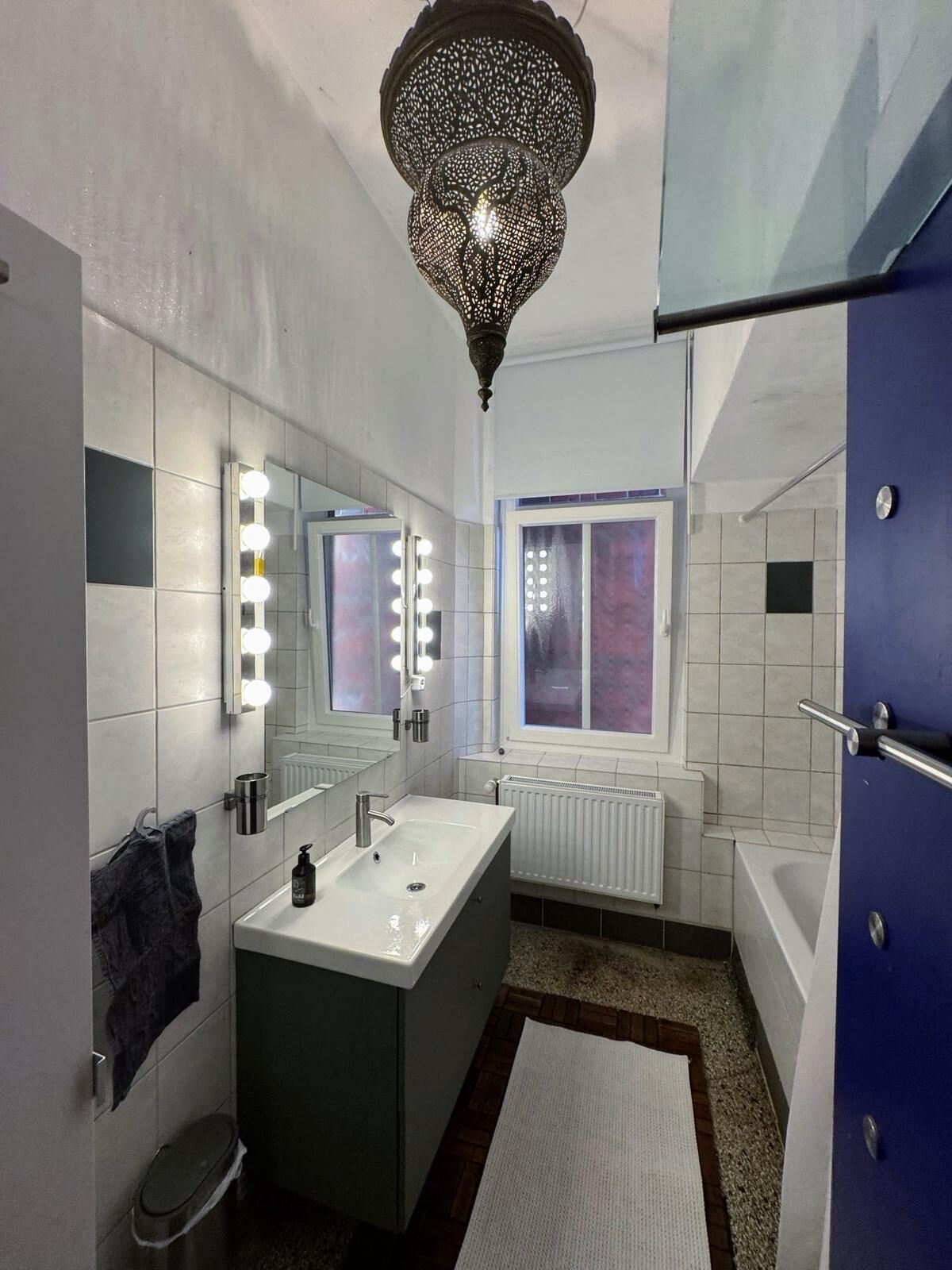 Ein modernes Badezimmer mit Waschtisch, Spiegel mit Beleuchtung, Heizkörper und einer blauen Tür.