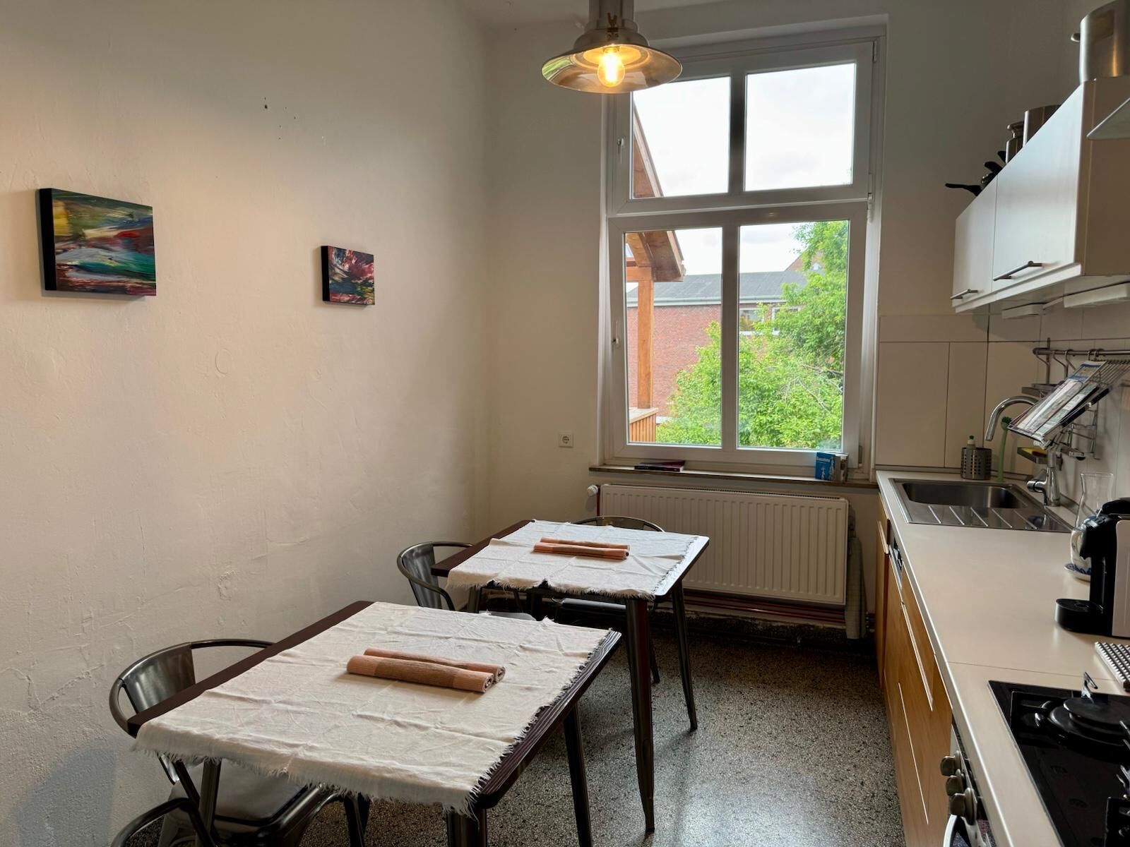 A kitchen with a window, a table with a cloth, and a chair.