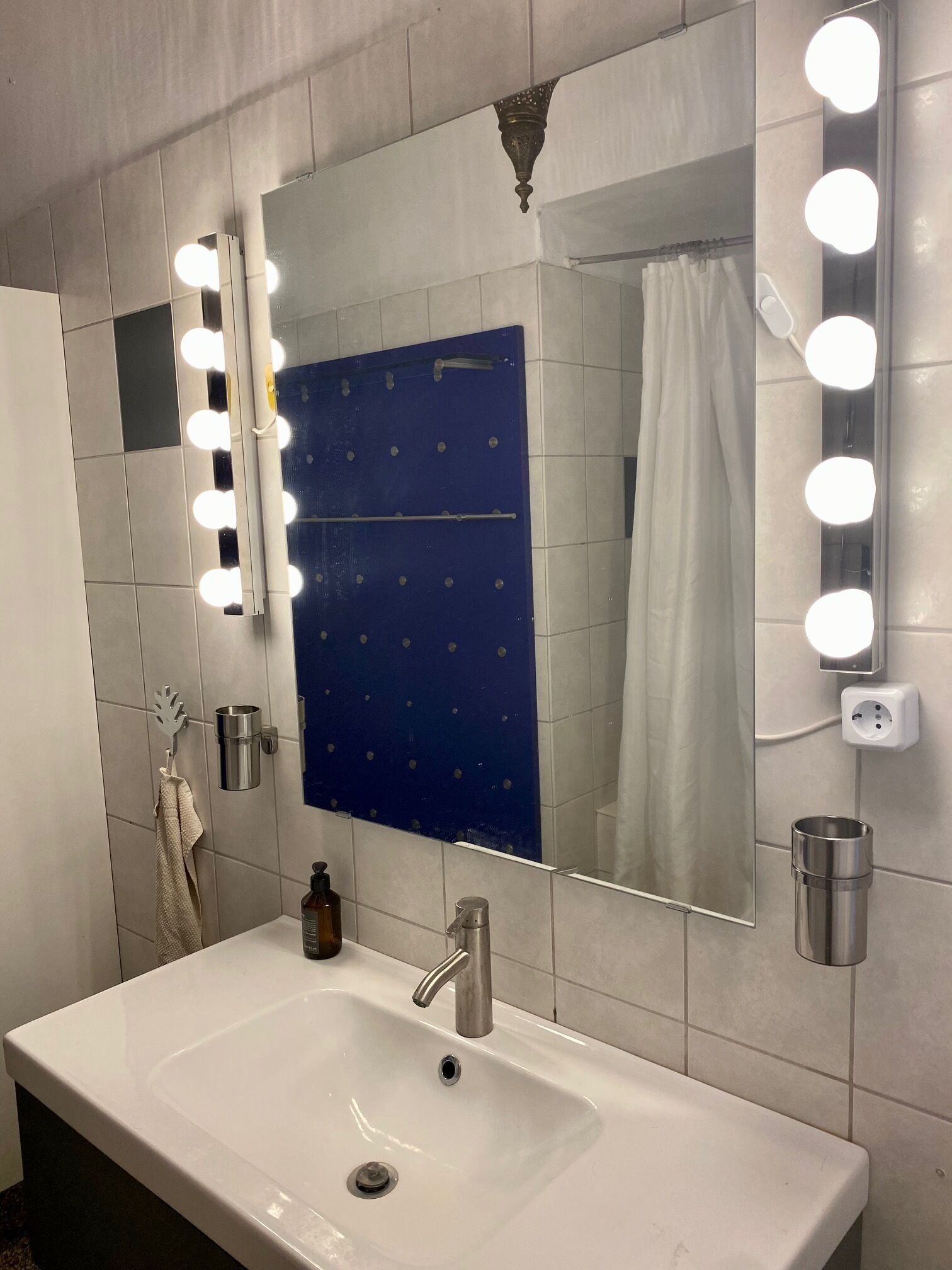 A bathroom with a large mirror, lights, a sink, and a towel rack.