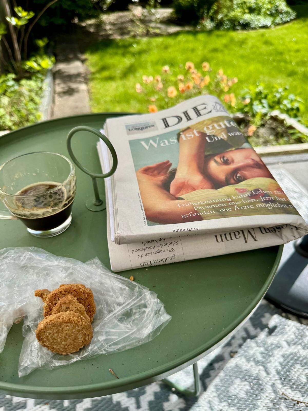 Un tavolo con un giornale, un bicchiere di liquido scuro e un panino impanato su un vassoio verde.