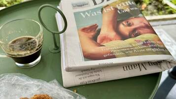 Un tavolo con un giornale, un bicchiere di liquido scuro e un panino impanato su un vassoio verde.