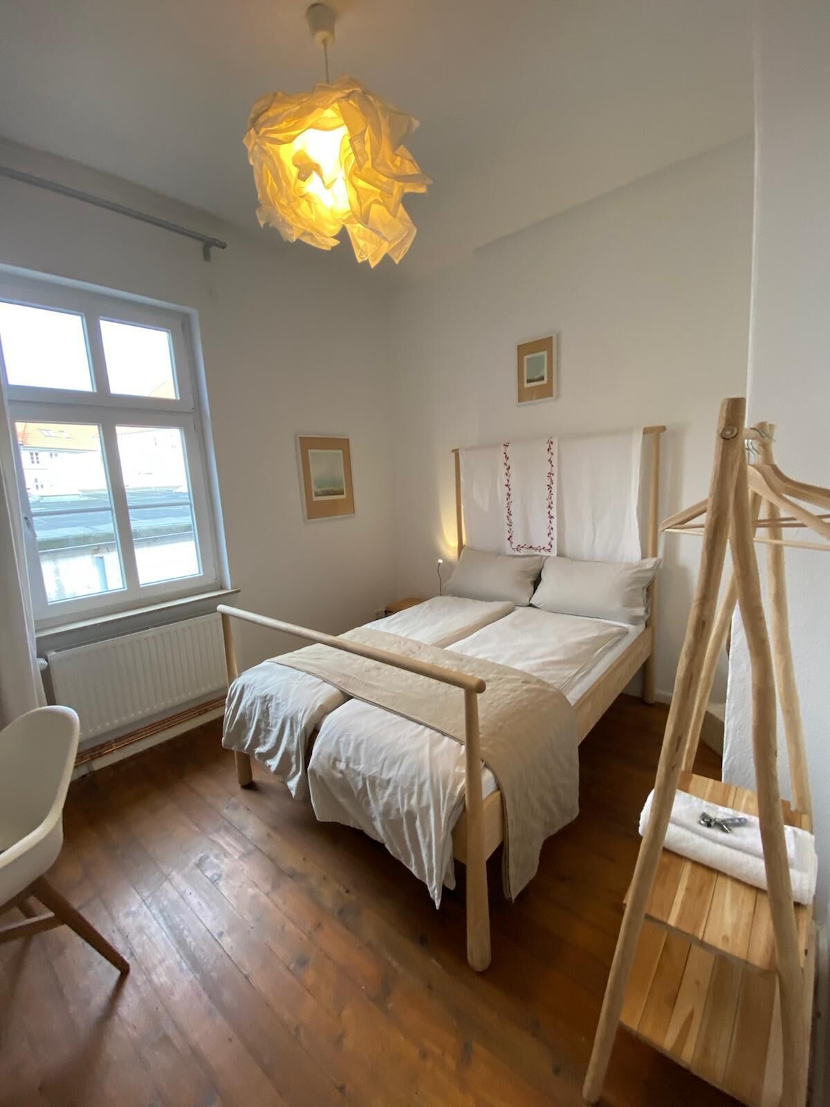Ein Schlafzimmer mit einem hölzernen Bett, einer Pendelleuchte, einem Fenster und einer Heizung.