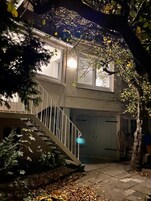 A two-story building with a staircase leading to the entrance, a garage door, and a tree in the foreground.