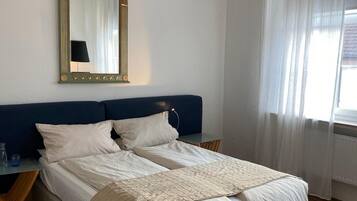 A bedroom with a bed, a nightstand, a chair, a large mirror, and a chandelier.