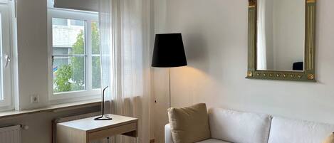 A hotel room with a bed, a desk, a sofa, a small table, a lamp, a mirror, and a decorative ceiling light.