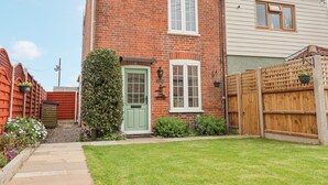 A two-story brick house with a green door, a small front yard, and a wooden fence. - 1 Rumsby Cottages (Lowestoft)