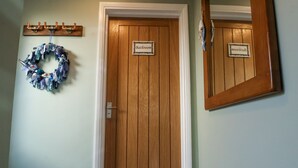 A wooden door with a sign reading "Bathroom" above it, a wooden coat rack with hooks, and a decorative wreath on the wall. - 1 Rumsby Cottages (Lowestoft)