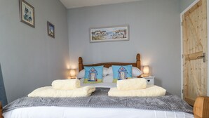A neatly made bed with white linens and two pillows, a wooden headboard, and two bedside lamps. - 1 Rumsby Cottages (Lowestoft)