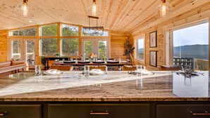 Una cabaña de madera espaciosa con una isla de cocina grande, varias mesas de comedor y amplias ventanas con vistas panorámicas.