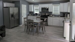 A modern kitchen with white cabinets, stainless steel appliances, and a dining area with wooden chairs. - Brand New Floating Home on Norris Lake : Sleeps 12 : Swim, Grill & Relax! #4 (LaFollette)