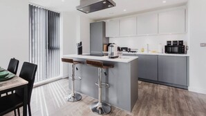 A modern kitchen with a central island, bar stools, and a dining area with a table and chairs. - Skyline Views | 2 Bed 2 Bath in Prime Location | Parking/Netflix! (Birmingham)