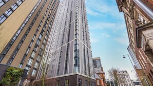 A tall, modern building with a glass facade, surrounded by other buildings. - Skyline Views | 2 Bed 2 Bath in Prime Location | Parking/Netflix! (Birmingham)
