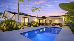 A modern house with a swimming pool, outdoor seating, and tropical plants.