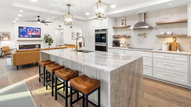 A modern kitchen with a large island, bar stools, a ceiling fan, and built-in appliances.