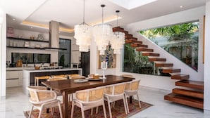 A modern kitchen with a dining area, featuring a large wooden table, wicker chairs, and a chandelier. - Luxury Villa Devina I Seminyak I Pool, Yoga & Gym (kerobokan Kelod)