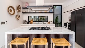 A modern kitchen with a central island, black appliances, and wicker bar stools. - Luxury Villa Devina I Seminyak I Pool, Yoga & Gym (kerobokan Kelod)