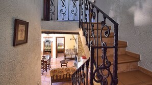 A staircase with ornate black railings leading to a second-floor landing. Below, a dining area with a table and chairs is visible. - Authentic cortijo with private pool (Loja)