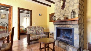 A cozy living room with a stone fireplace, a floral sofa, and a dining table with chairs. - Authentic cortijo with private pool (Loja)