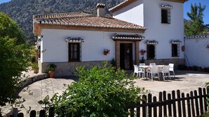 A two-story building with a tiled roof and white walls, featuring a patio with outdoor seating and potted plants. - Authentic cortijo with private pool (Loja)