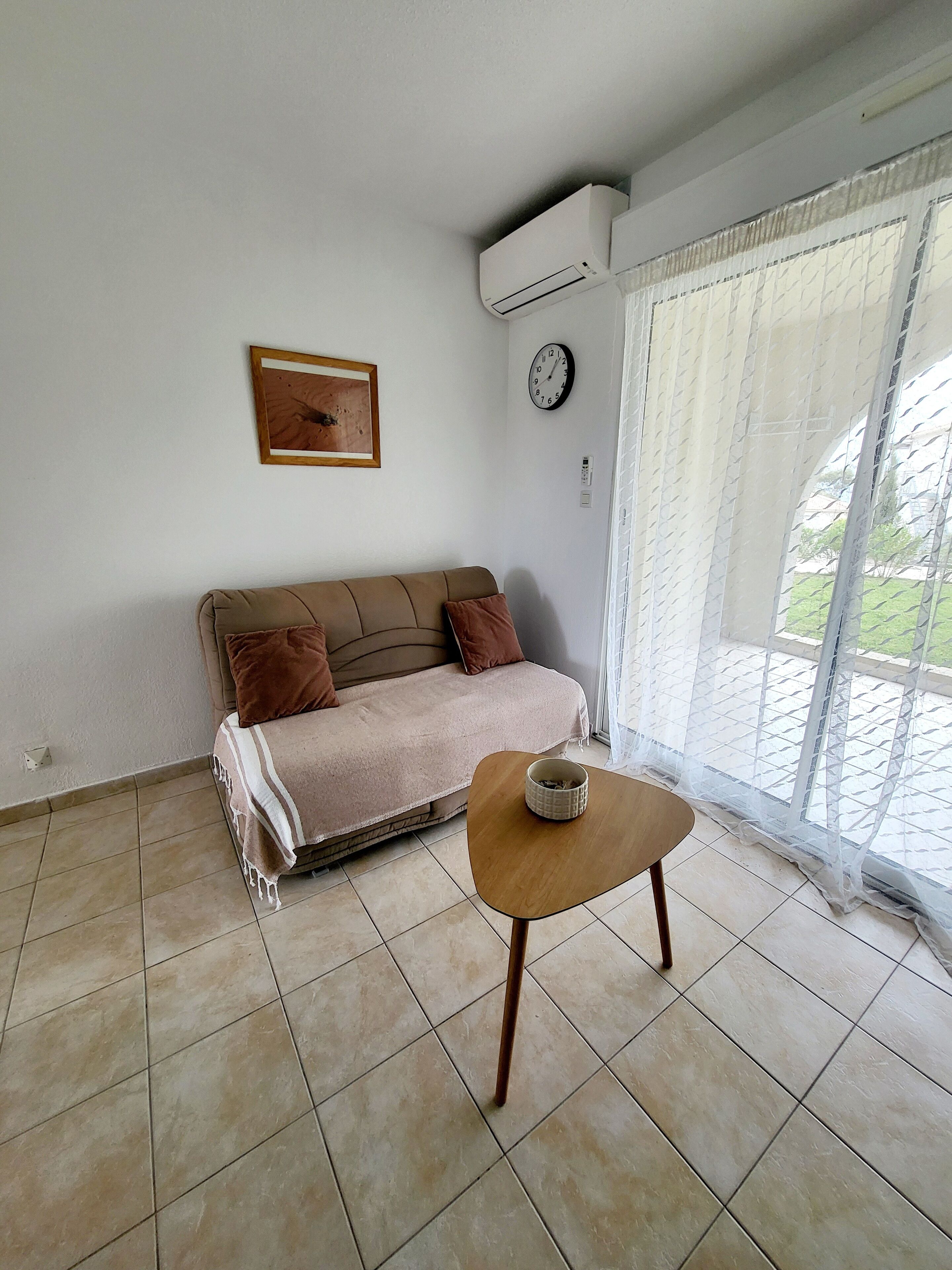 Una sala de estar con un sofá, una mesa de centro, un reloj y una ventana con cortinas.