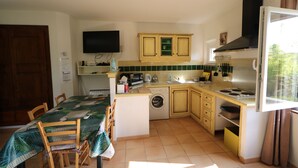 Cocina compacta con microondas, lavabo y estufa. Hay una mesa de comedor con sillas y una lavadora.