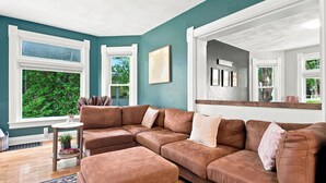 Un salon avec un canapé d’angle, une petite table d’appoint ornée d’une plante, et une vue sur la verdure à l’extérieur.