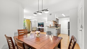 A dining area with a wooden table and chairs, a vase of flowers, and a kitchen in the background. - Cozy 1 bedroom +1 bathroom condo in enchanting Miami with AC, WiFi, Fitness room (Miami)