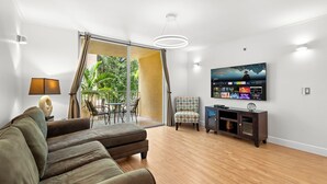 A modern living room with a large flat-screen TV, a sofa, a patterned armchair, and a wooden floor. - Cozy 1 bedroom +1 bathroom condo in enchanting Miami with AC, WiFi, Fitness room (Miami)