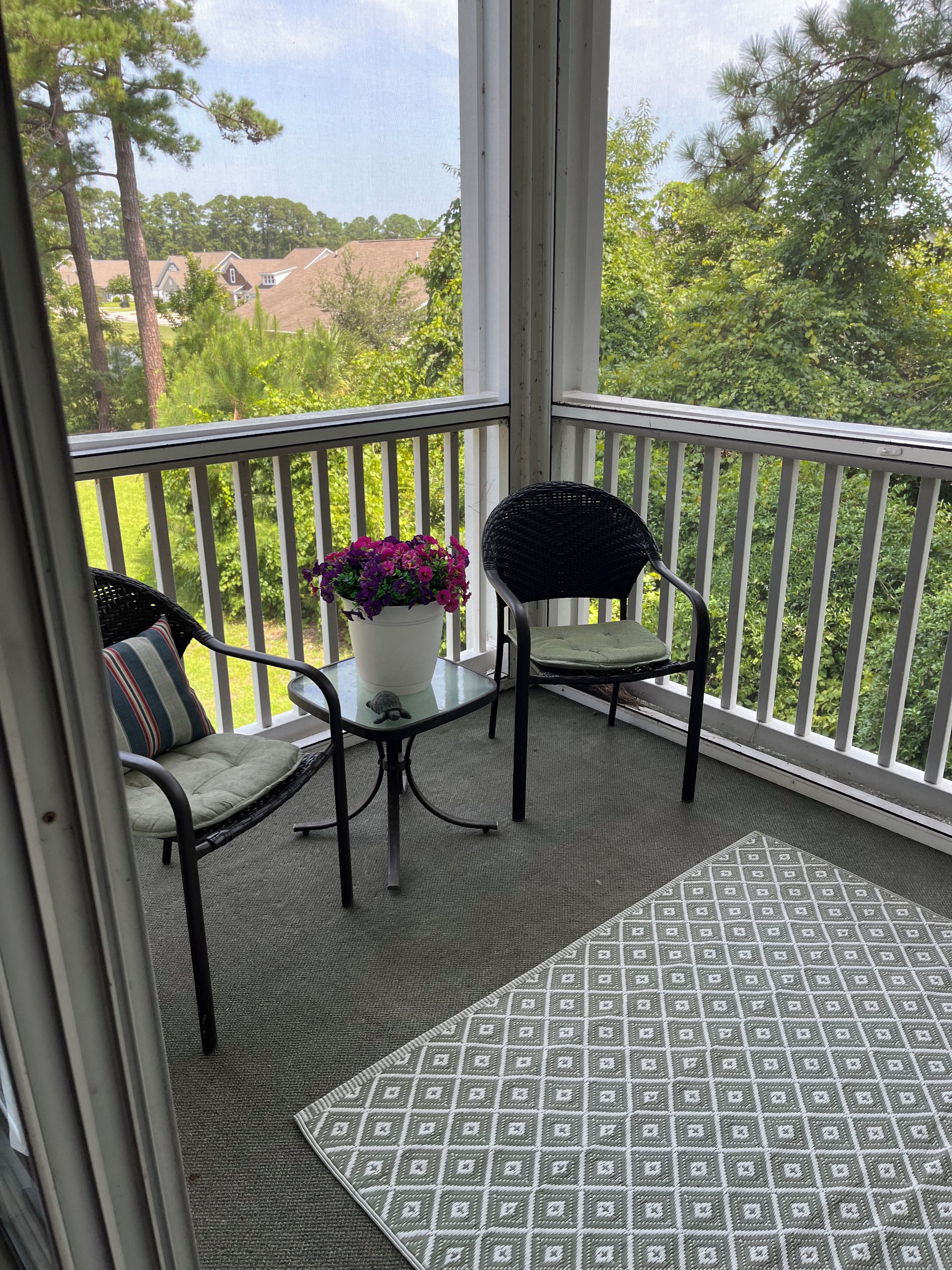 A balcony with a view of a residential area, a potted plant, and two chairs.