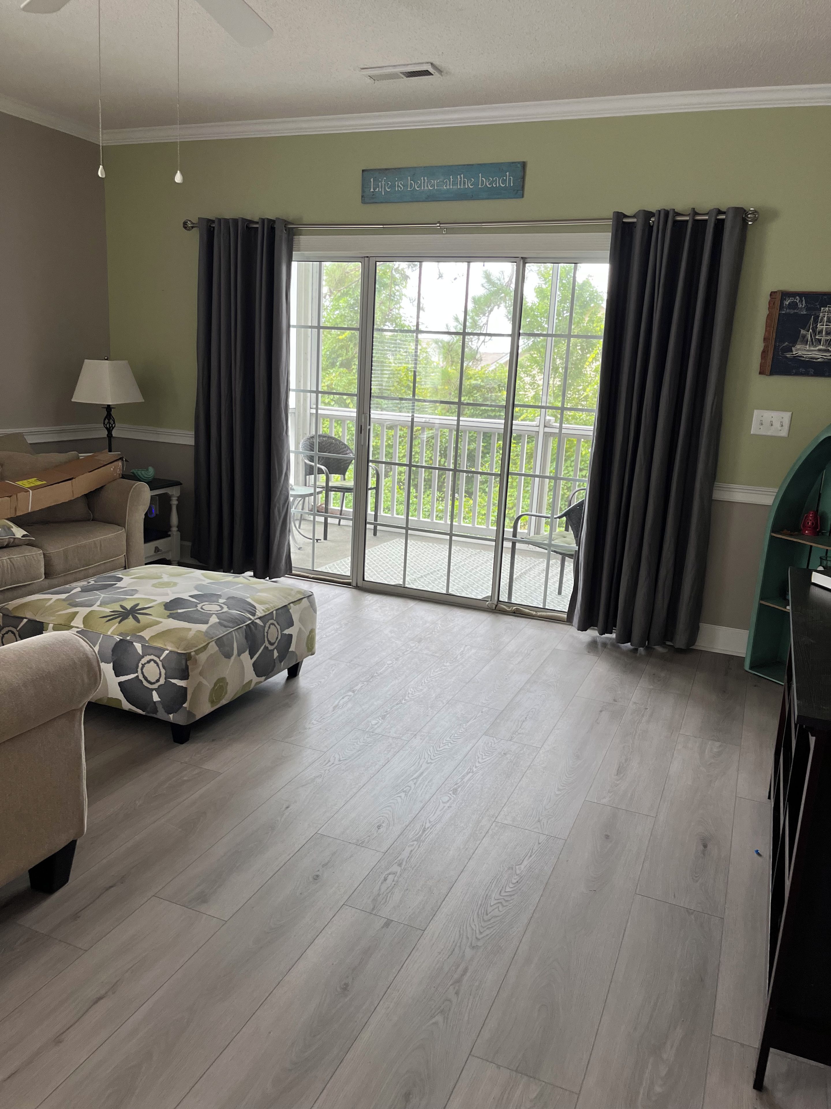 Una sala de estar con sofá, reposapiés y vista a un balcón con cortinas.