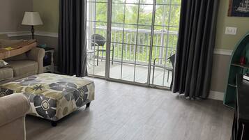 Una sala de estar con sofá, reposapiés y vista a un balcón con cortinas.