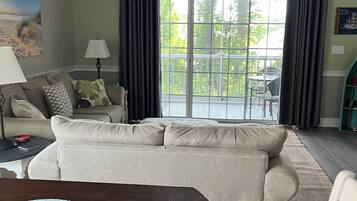 A living room with a sofa, a dining table with a placemat, a ceiling fan, and a view of the outdoors through a sliding glass door.