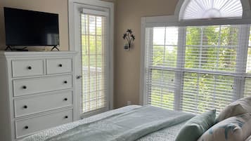 A bedroom with a bed, a dresser, a television on top, and a window with blinds.