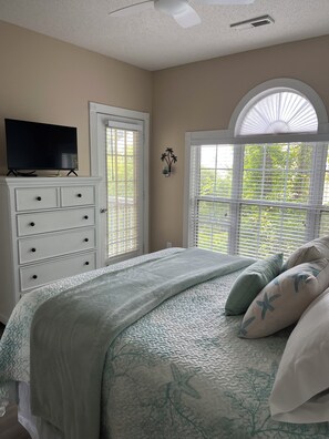 A bedroom with a bed, a dresser, a television on top, and a window with blinds.