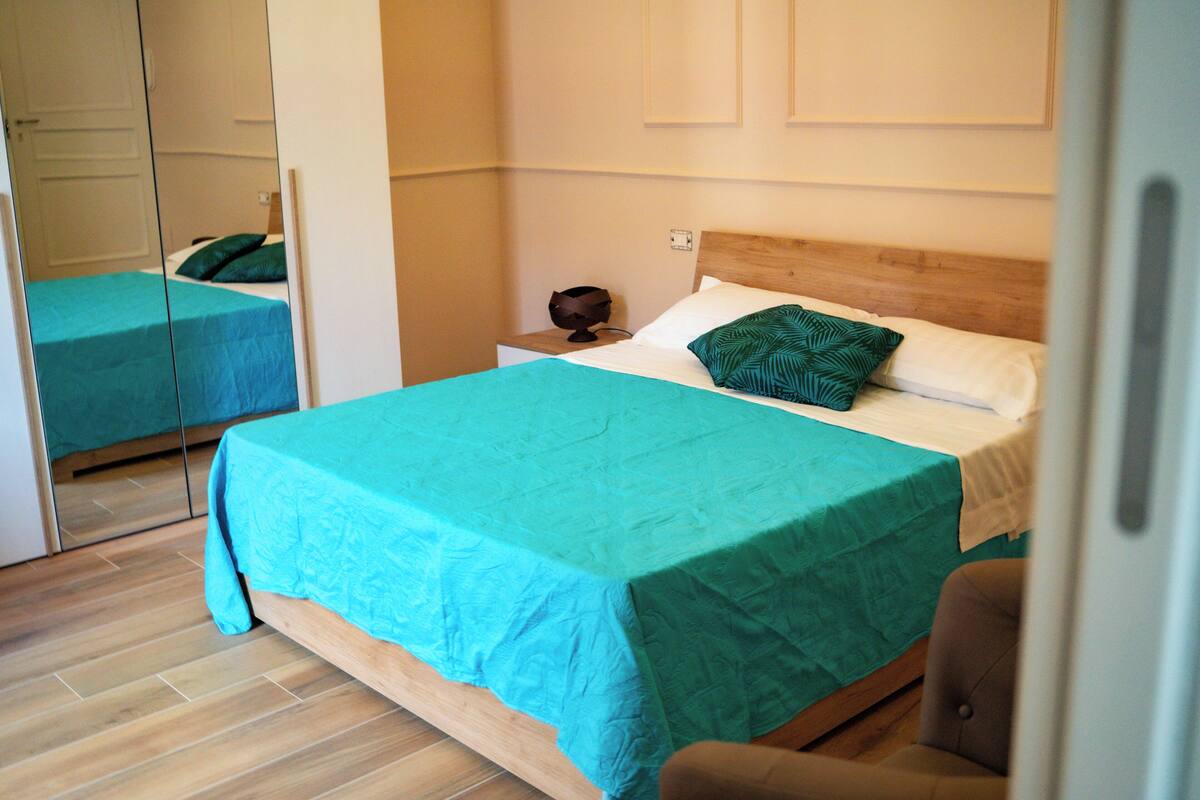 Un dormitorio con cama, una silla, una mesita de noche y un espejo.